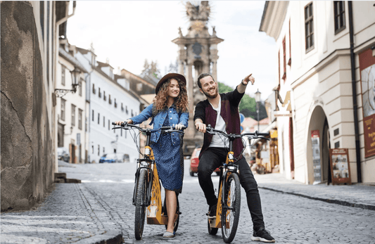 Two people with yellow electric bikes on a cobblestone street in a city setting, front view