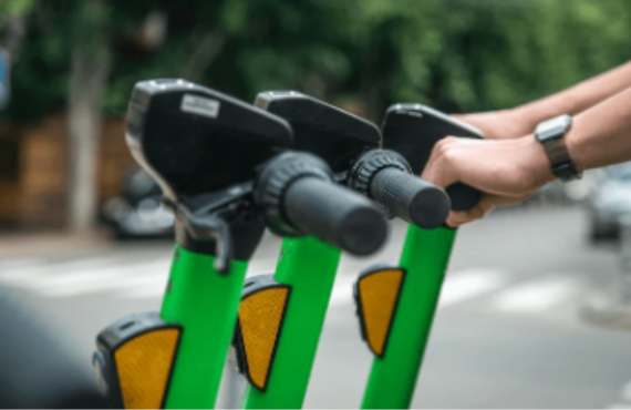 Person gripping handlebars of green electric scooters on city street, Pogo Cycles e-scooters