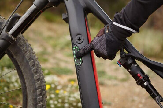 Close-up of gloved hand pressing battery indicator on electric mountain bike at Pogo Cycles