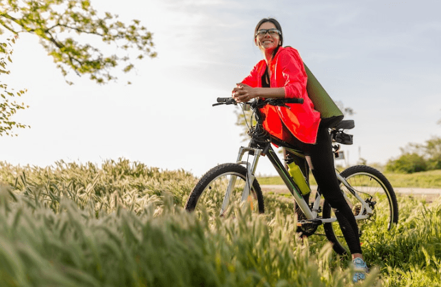 Woman with electric bike in green field, wearing red jacket, Pogo Cycles outdoor e-bike ride
