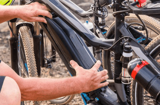 Person installing battery on electric bike frame outdoors, showcasing Pogo Cycles e-bike quality.