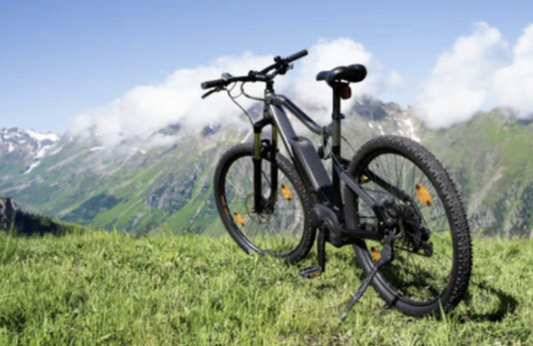 Black electric mountain bike side view on grassy hill with scenic mountain background