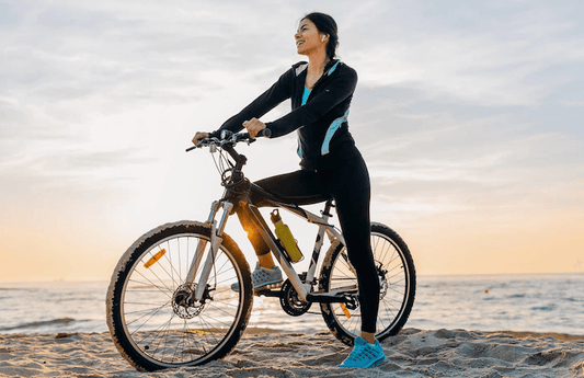 Woman riding an electric bike on the beach at sunset, Pogo Cycles e-bike lifestyle scene