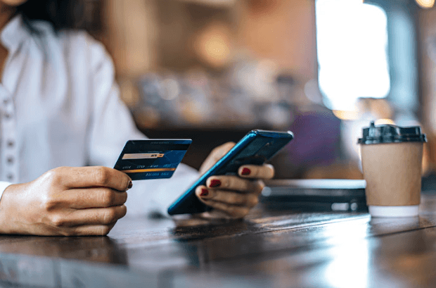 Person holding credit card and smartphone making online payment at a cafe table